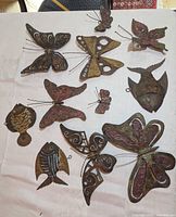 Top-down view of a collection of metal butterflies and fish wall hangings on a white cloth.