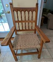 Front view of the armchair showing the medium stained pine wood with turned spindle backrest and woven sisal seat.