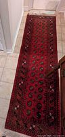 Overall view of red runner rug on tile floor showing full length and pattern