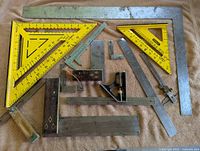 Shows the complete assortment of different types of square measuring tools including plastic, metal, and wooden handled pieces arranged on a surface