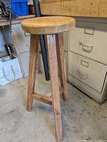 Full view of the round topped wooden shop stool standing on the floor showing legs and seat.