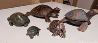 Group photo of five turtle figurines of various materials including stone, wood, and paper mache showing size and detail.