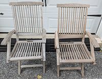 Front view of two teak folding chairs with arms showing slatted back and seat design and natural weathered finish.