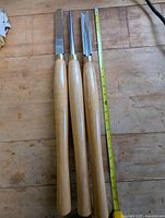 Three chisels laid out flat beside measuring tape showing length of about 23 inches.