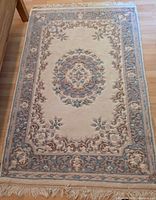 Full view of wool oriental carpet showing the central floral medallion, ornate border, and fringed ends on wooden floor.