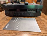 Front view of Yamaha RX-490 RX-399 home theatre receiver unit with user manual and power cable on top placed on a wooden table.