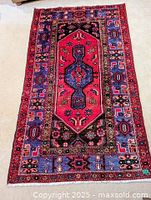 Full view of rug laid flat on floor, showing red central medallion, black inner field, purple outer border and fringe.