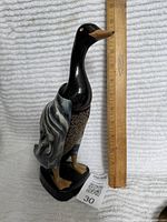 Front view of the black plastic duck holder standing next to a ruler showing approximately 11 inches tall, highlighting the detailed body and marbled wings.