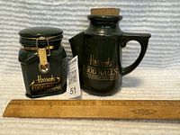 Photo of both Harrods green containers side by side with a ruler showing scale, one square snap-lid canister, one corked jug with cork stopper.