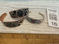 Front view of all three bracelets showing etched designs on copper cuffs and inset on metal cuff