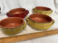 Four glazed pottery bowls arranged with measurement ruler, showing size and glaze colors of red and yellow terra cotta style.