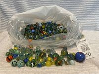 Large assortment of vintage glass marbles in a plastic bag and laid out on a towel showing a range of sizes and colors including large blue and orange marbles.