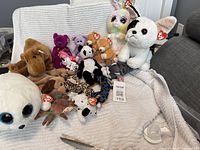 Full lot of vintage Ty Beanie Babies plush animals arranged on a beige textured blanket; various animals and sizes visible with tags.