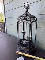 Front view of metal lantern candle holder showing height with measuring tape and intricate top scrollwork