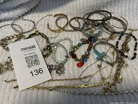 Photo of multiple bracelets including metal bangles, beaded, and charm bracelets laid out on a textured surface with a MaxSold support tag number 136 included in image
