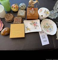 Image showing a range of vanity items including porcelain dishes with floral patterns, decorative trinket boxes, a small wooden box, glass angel figurine, crystal perfume bottle, and a boxed collectible from Metropolitan Museum of Art, New York.