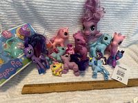 Photo showing 11 assorted My Little Pony figures in varied colors, a ruler for size reference, and a sealed Peppa Pig tea set package.
