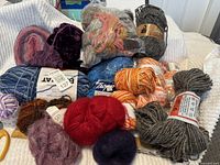 Multiple skeins and balls of yarn including 100% virgin wool, cotton, and carded soft pure wool for crafting purposes.
