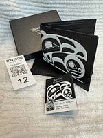 Photo showing the black leather wallet with white and black Raven design, box labeled with Roy Henry Vickers name, informational card and cloth pouch.