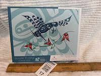 Box front showing puzzle artwork of Indigenous bird design in blues and reds, with text indicating 1000 pieces and artist.