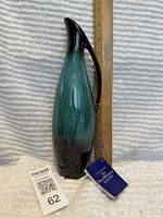 Front view of vintage Blue Mountain Pottery tall jug with original blue and white tag, next to a wooden ruler for size reference showing approximately 11 inches tall.