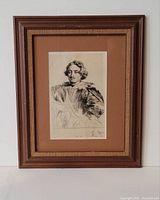 Framed engraving in a wooden frame with brown matting shown full front view.