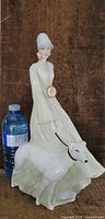 Full view of Royal Doulton figurine 'Reflections' showing woman in long dress seated with white Greyhound dog, next to a water bottle for size reference.