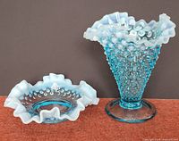 Photo of Fenton blue opalescent hobnail trumpet vase and matching bowl on carpeted surface showing ruffled edges and hobnail pattern.