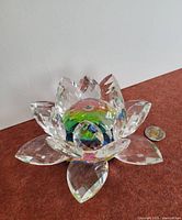 Crystal flower figurine with clear faceted petals surrounding a colorful spherical center, placed on a flat surface with a coin beside for scale.
