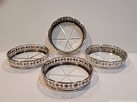 Four Birks sterling silver coasters grouped together showing the decorative openwork floral pattern and glass inserts.