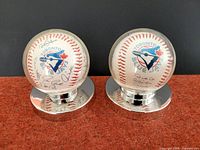 Front view of two Toronto Blue Jays baseballs with printed autographs, displayed on circular mirrored bases.