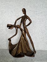 Front and side view of the abstract bronze sculpture showing the man and woman figures in dance pose with flowing dress details.