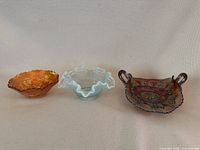 Photo of the three carnival glass bowls side by side on a plain surface, showing varying colors and shapes.