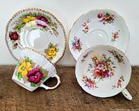 Two porcelain teacups and saucers with floral designs; one pair with pansy-like flowers in yellow, pink, purple and gold trim; the other pair with mixed small floral designs in pink, red, yellow, purple and subtle gold trim