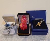 Jewelry lot showing several brooches in boxes including a red crystal sculpture and Swarovski brooch