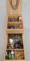Full view of the wooden jewelry organizer showing assortment of necklaces, bracelets, rings, watches, and brooches in compartments.