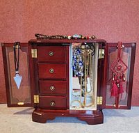 Full view of wooden jewelry box open showing drawers, hanging necklaces and pendants on mirrored doors.