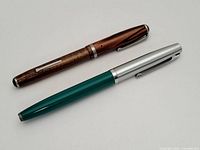 Pair of two fountain pens shown including a brown marbled finish pen and a green and silver two-tone pen.
