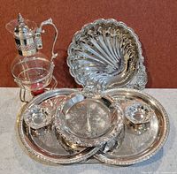Full view of the silver plated collection including glass pitcher with silver plated lid and stand, two-tier tray, oval tray, shell dish, and two small bowls.