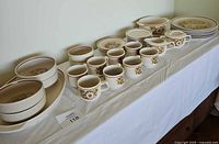 Overview of the whole dish set displayed on a white cloth, showing multiple cups, bowls, plates, and serving pieces arranged in rows