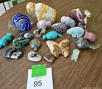 Group view of all carved stone and glass animal figurines spread out on surface with auction lot number card