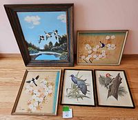 Overall view of five bird and waterfowl artworks including paintings and prints displayed on a wooden floor against a pink wall.