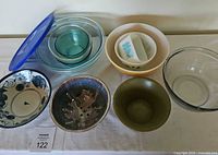 Overview of eight bowls arranged on table including vintage and modern Pyrex glass bowls, hand thrown ceramic bowl with drainage holes, and other glass and ceramic bowls