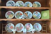 Twelve Franklin Porcelain decorative plates arranged on wooden shelves along with Royal Standard teacups and saucers and two rustic twig stands