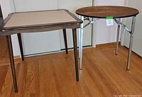 Two folding tables side by side, square card table with vinyl top and round wood King Arthur table with metal legs