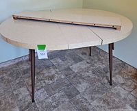 Vintage round kitchen table with removable leaves shown from an angle, displaying speckled off-white Formica surface and three tapered legs.
