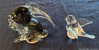 Photo of the Murano Italy glass rabbit figurine and Great City Traders sparrow paperweight on dark cloth background.