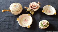 Lot showing Lenox jewelry dish, Andrea by Sadek rose figurine, two Schumann Arzberg ashtrays, and Arnart Creation silent butler on fabric background