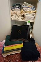 Photo showing a pile of various linens including sheets, multiple bath towels and rags, and a prominent black wool blanket with monogrammed 'F' on top.