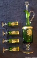 Green blown glass decanter with clear stopper and gold rim along with four matching green glasses with gold rims and emblems